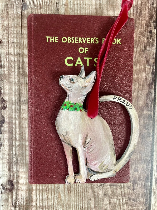 Hairless Sphynx Cat Christmas Decoration strung with red velvet ribbon and placed on a green book