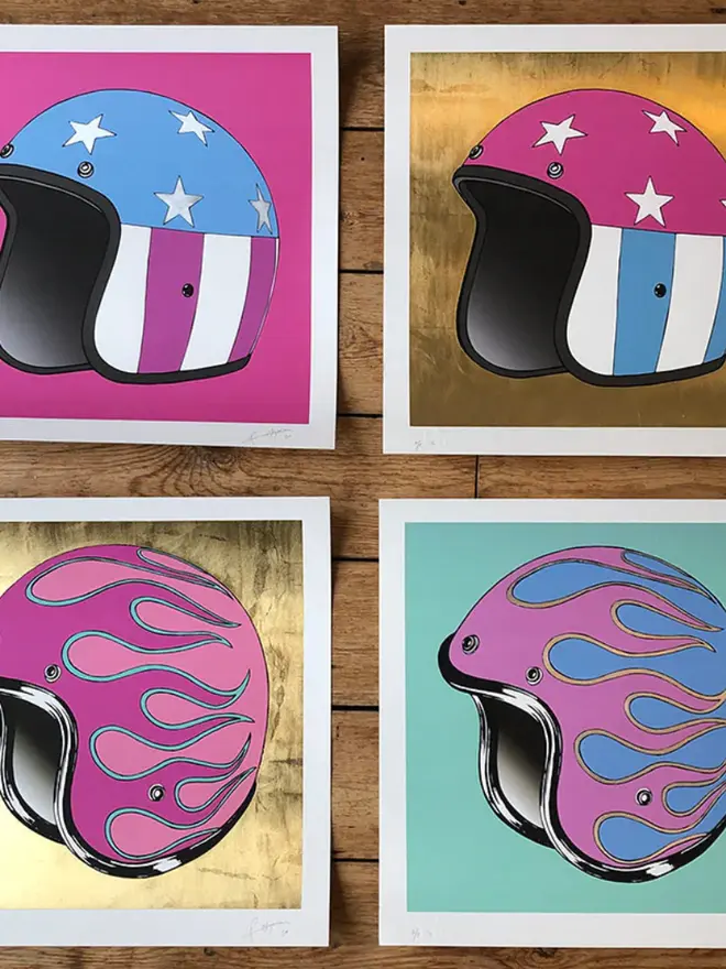 Four square art prints of motorcycle helmets. Two show a star-and-stripe design on pink and gold backgrounds; two show a flame design on gold and teal backgrounds.
