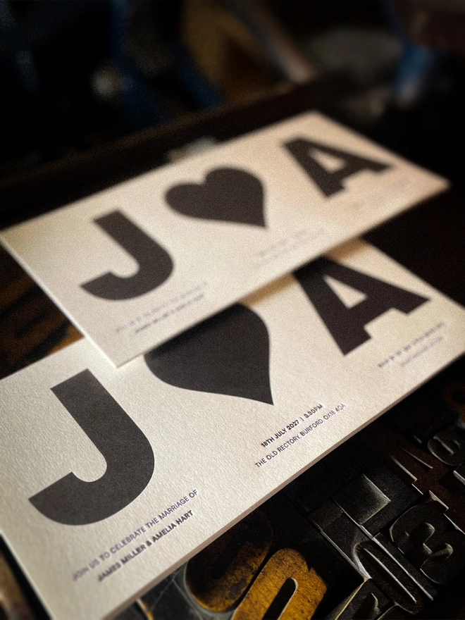 Modern monochrome concertina wedding invitation shown folded and open, personalised with oversized initials, heart, wedding date and venue details in black letterpress ink.