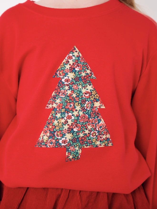 a 5 year old girl wearing a red t-shirt with a liberty floral christmas tree sewn on to the front