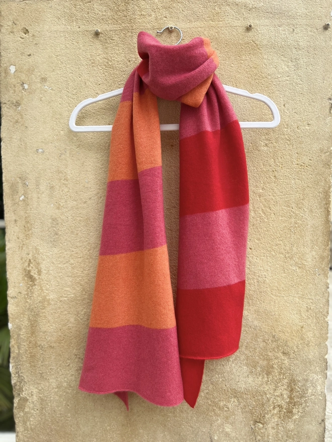 Red pink Orange scarf shown on a hanger against a wall