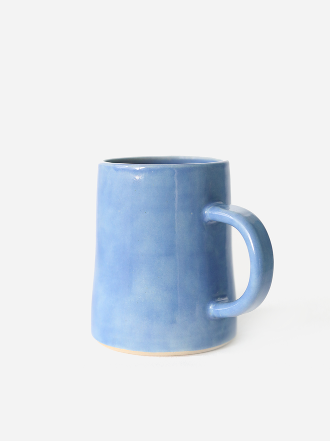 A handmade ceramic pint mug in pacific blue glaze with a chunky loop handle, photographed against a plain light grey background