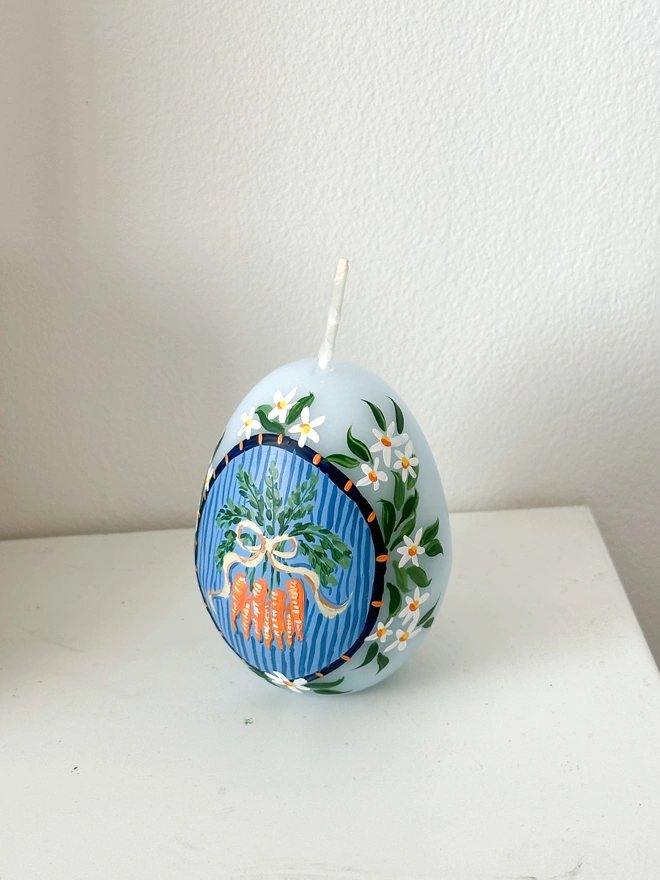 Hand Painted Easter Egg Candle Carrots Bunch, an Easter egg candle sitting on a plain surface. It's Easter and floral design wraps around it. 