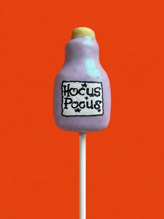 Lilac potion bottle cake pop on a white stick against a bright orange background