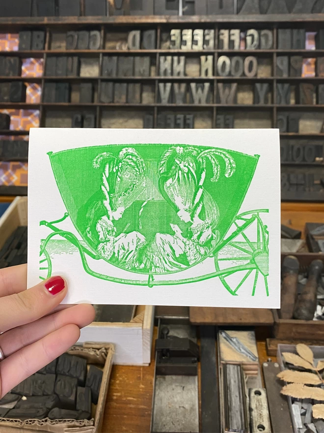 Hand holds up white greeting card with a printed green illustration and text.