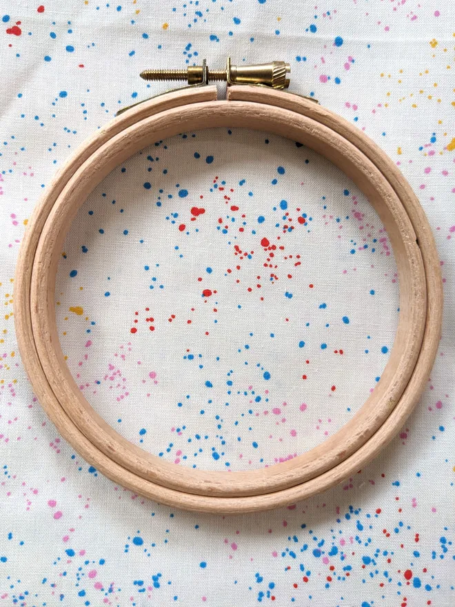 A wooden embroidery hoop lying on fabric with a rainbow speckles design