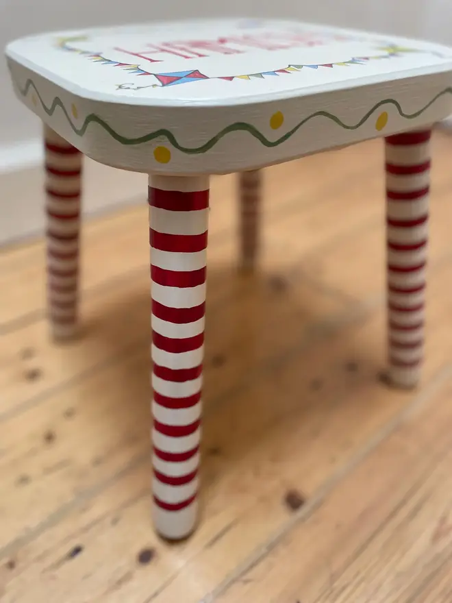 personalised hand-painted nursery stool. a small white stool with red and white striped legs, photographed from the side.