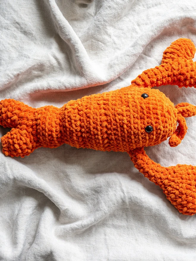 Chunky Chenille Cuddly Crochet Crustacean Lobster Plush, an orange lobster plush sitting on a white table cloth. 