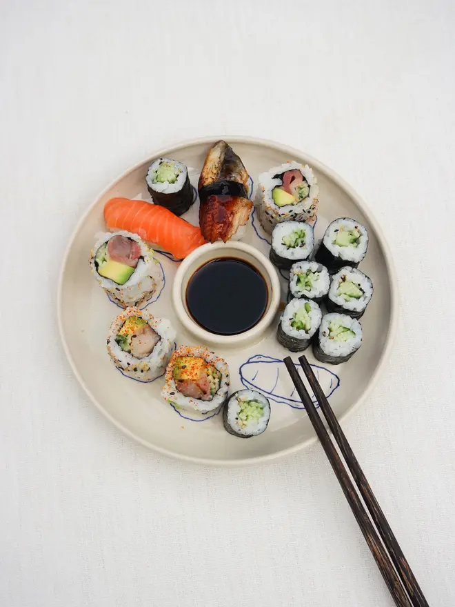 Snack Sushi Dippy Plate, a sushi snack dish sitting on a white surface. It is accompanied by sushi and chopsticks