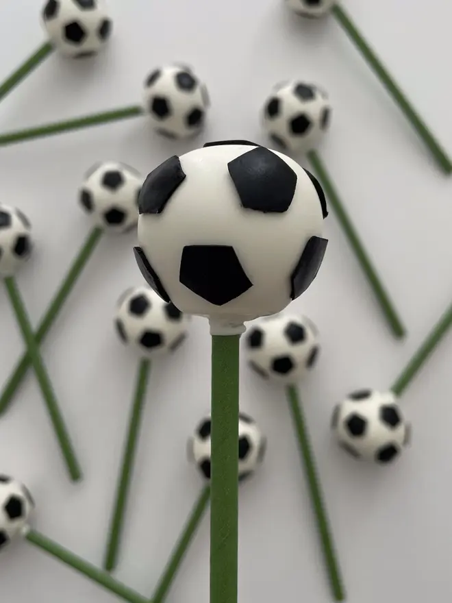 Football Cake Pops (Pack Of 6, 12, 18, 24), football cake pop placed into a cake in front of a background of more cake pops. This is against a white surface. 