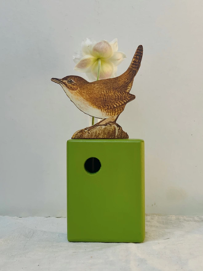 A tiny wren perched on a recycled wood block, painted green with a glass test tube bud vase