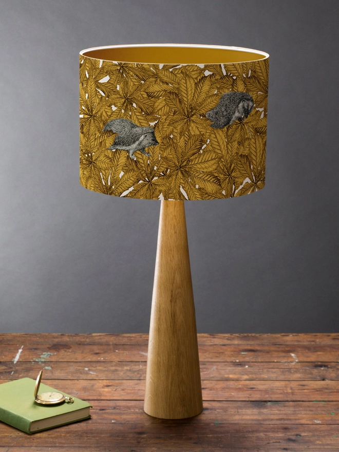 Handmade lampshade featuring cosy hedgehogs nestled among autumnal yellow leaves, creating a warm and whimsical woodland design.