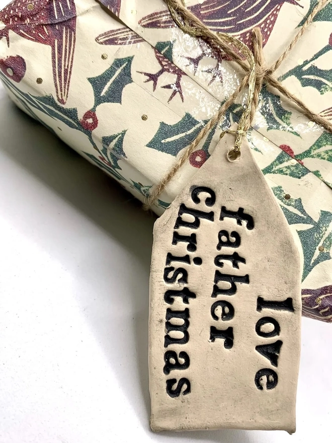 'Love Father Christmas' Handmade Ceramic Gift Tags, a ceramic gift tag attached to a gift sitting on a plain white surface. 