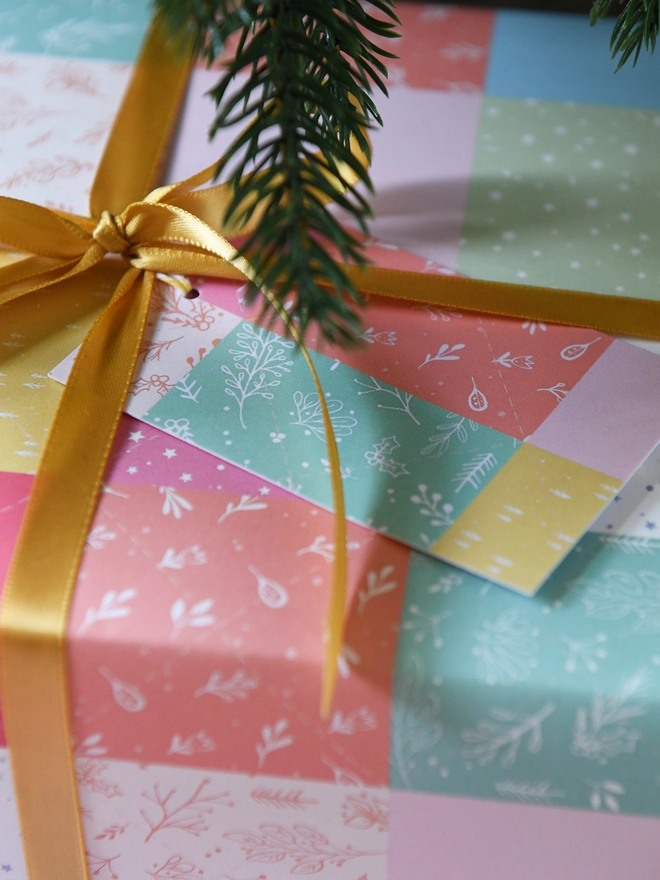 Gifts wrapped in gift wrap with a design of pastel patchwork quilt design is tied with gold ribbon.