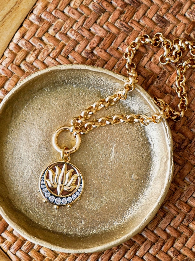 Gold lotus medallion charm inside a gold dish on a rattan background