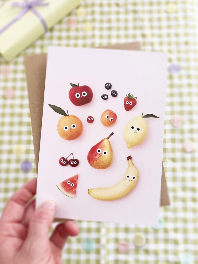 A lady holding a fruit friends card. over a green gingham party table. 