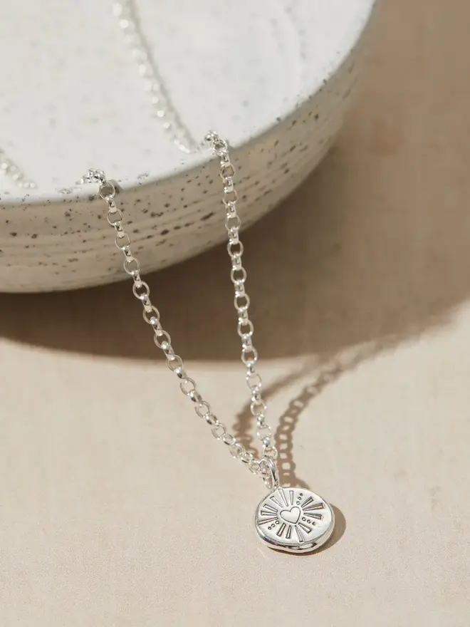 Silver Darling Heart Pebble Necklace draped over a bowl