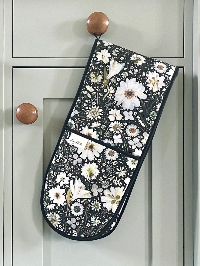 Floral double oven gloves with pressed white flower design on a black background. Complete with hanging loop.