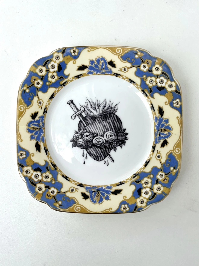 a vintage plate with an ornate border, the centre is white and printed on that is a black illustration of a sacred heart