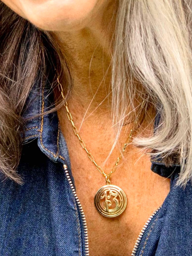 Close up on a woman with grey hair wearing a gold paperclip chain necklace with a number 13 charm 