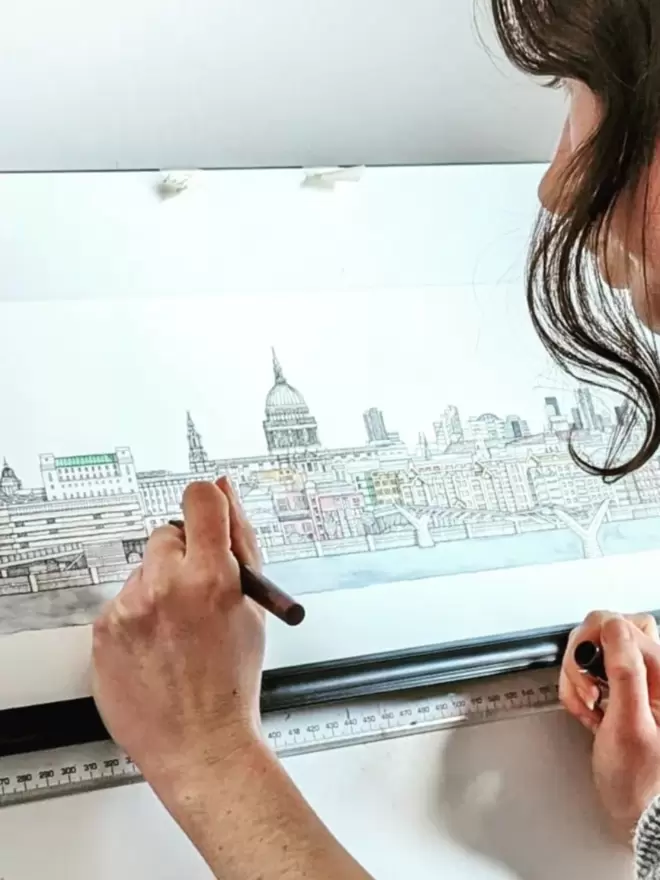 Artist Katherine Jones using a pen to hand-draw St Paul’s Cathedral and surrounding buildings 