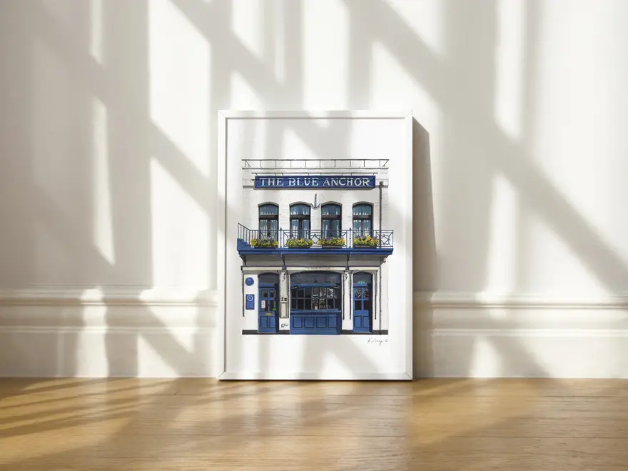 Hammersmith The Blue Anchor Giclée Print (Unframed), a print of a blue pub sitting in a white frame on a wooden surface against a plain backdrop. 