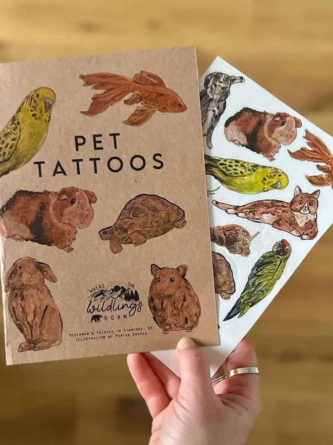 Pets Temporary Tattoos, A hand holds two brown kraft paper tattoo booklets titled "CAT TATTOOS" and "DOG TATTOOS."