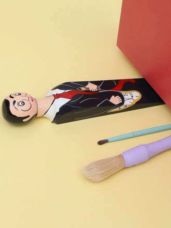 Wooden Door Stopper (Salvadoor), a colourful wooden door stop sitting under a door.
