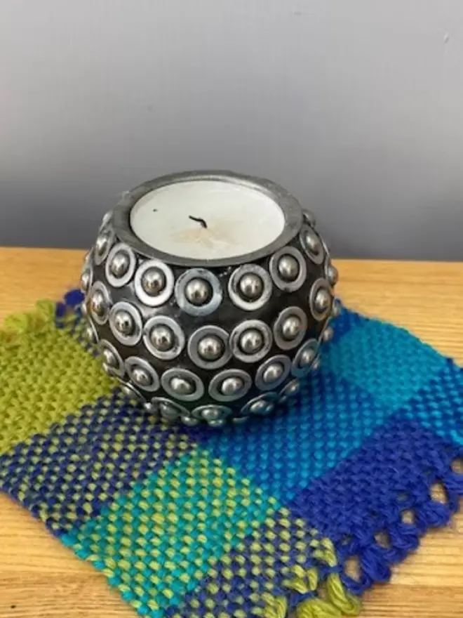 Square weave blue, teal, and yellow woven sample, matching yarn skeins, on a wooden table. 