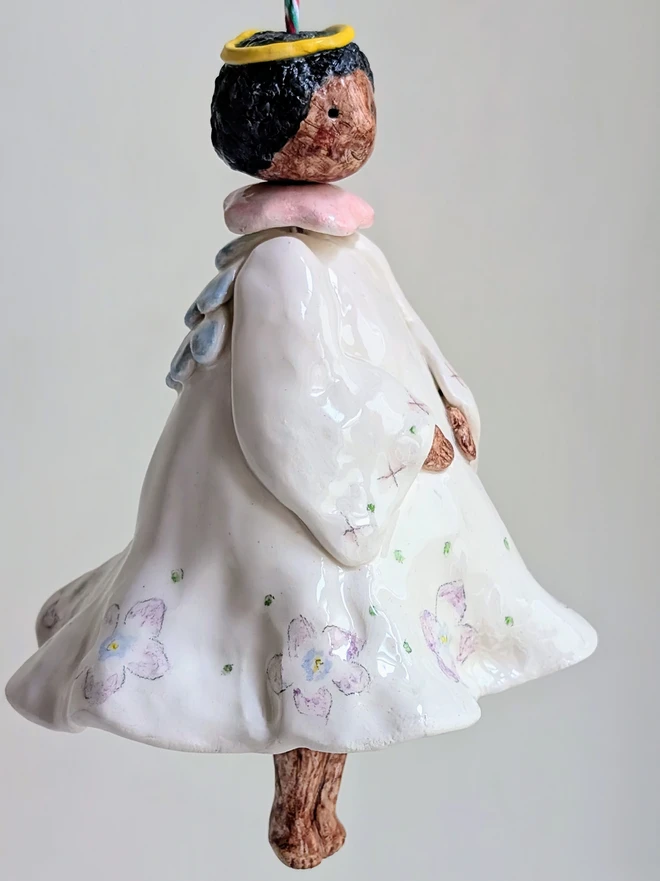 a hanging angel bell decoration with brown skin and violet floral dress in handmade white ceramic