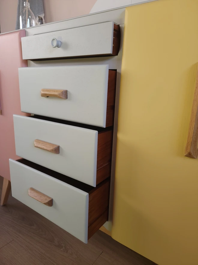 Four slightly open drawers on a pink, beige and yellow painted sideboard
