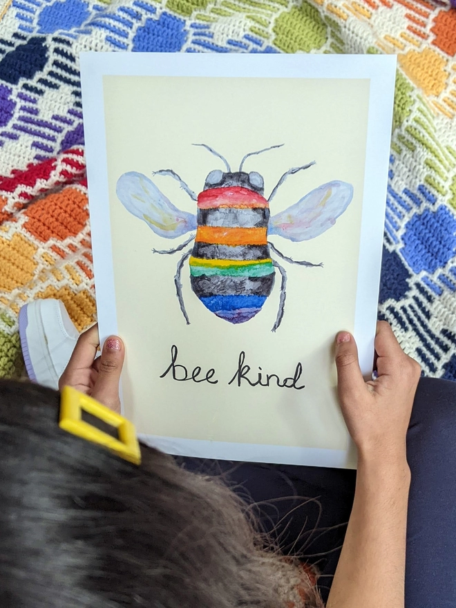 Young girl sitting holding an art print saying 'Bee kind'