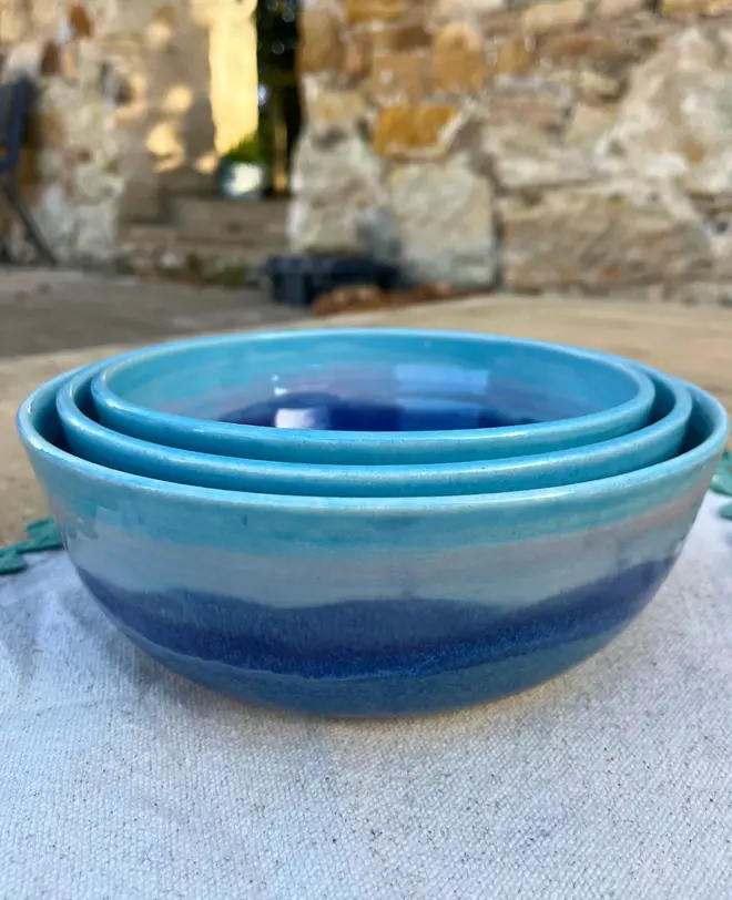Landscape Serving Bowls (Set Of 3), a collection of colourful serving bowls on a wooden table with a brick backdrop. 