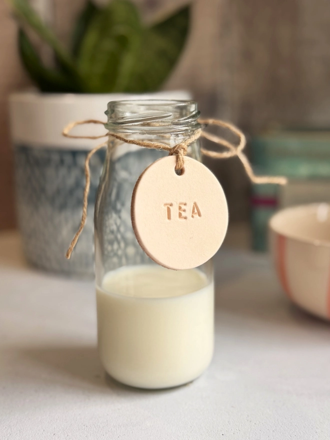 Rustic leather tag hand-stamped with "TEA", tied with jute twine on a glass bottle. Perfect for farmhouse kitchen décor, pantry organisation, or personalised gifting