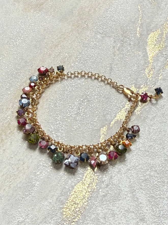 golden chain bracelet with rainbow jewel charms sitting on white surface