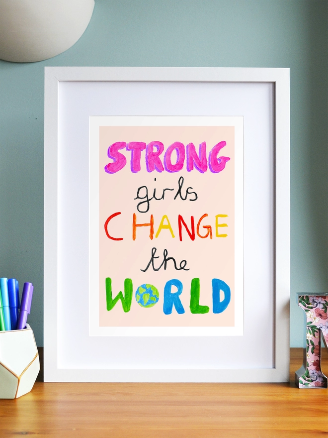Art print saying 'Strong girls change the world' in a white frame in a child's room