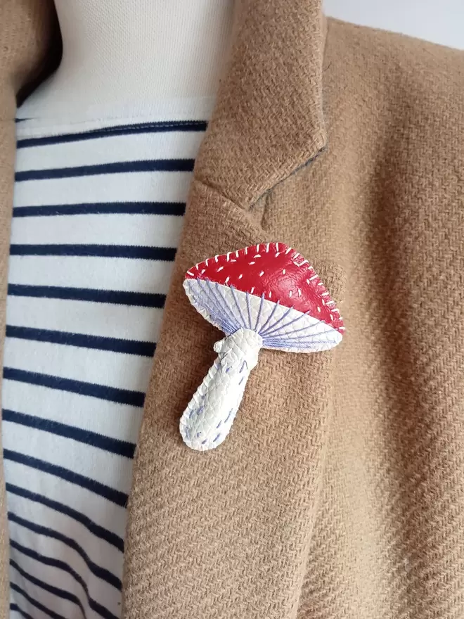 A red and white toadstool brooch pinned onto a camel coloured coat lapel