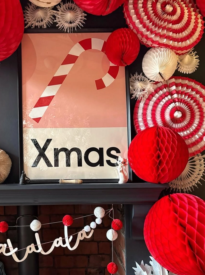 Framed Christmas wall print of a candy cane on pink background. Sitting on a black shelf surrounded by christmas decorations