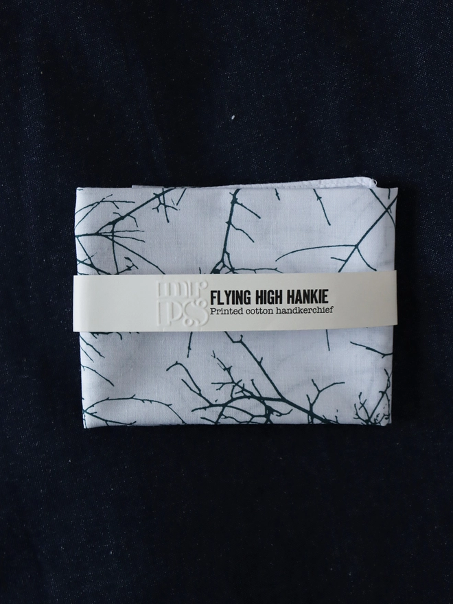 A Mr.PS Flying High Handkerchief folded with a paper label band on a denim tablecloth