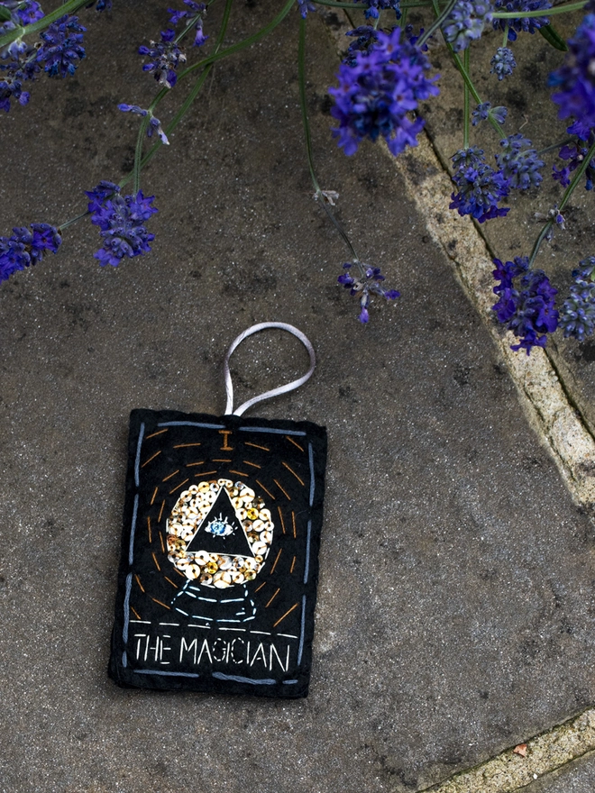 A handcrafted felt ornament with sequins and embroidery depicting "The Magician" tarot card. Colourful embroidery with an eye inside a crystal ball. 