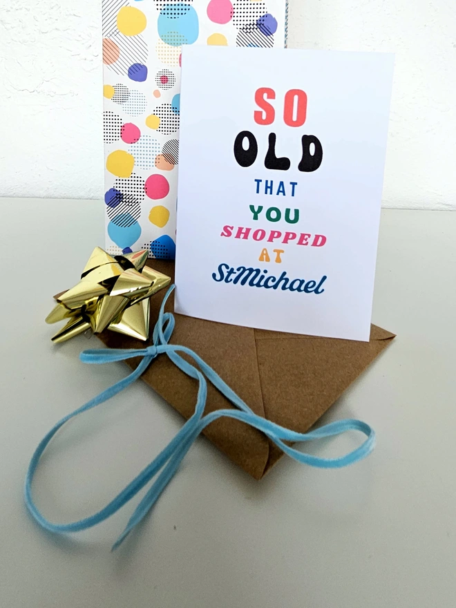 A photograph of the front of a humorous A6 greeting card illustrated using brightly coloured text and the retro shop logo. The text says so old you shopped at St Michael.