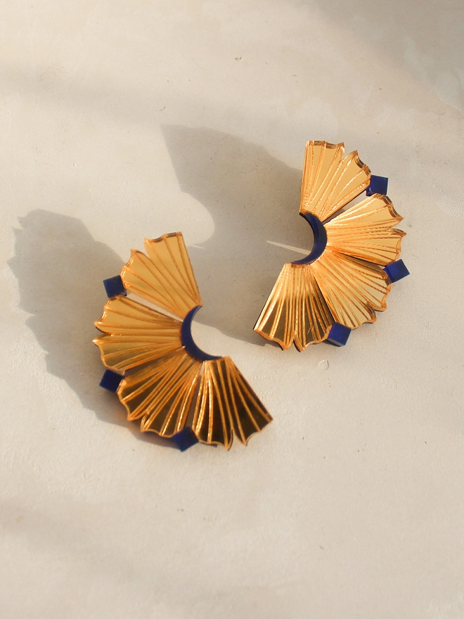A still life image of pair of earrings in gold and navy. The earrings resembles like the coral walls of Lamu Island and sliced pineapple.