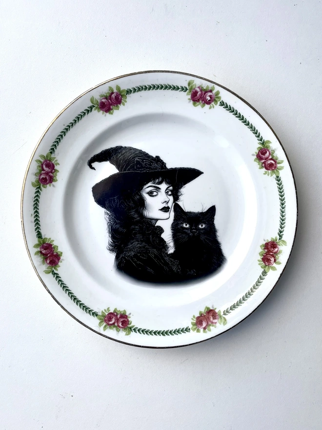 vintage plate with an ornate border, with a printed vintage illustration of a Victorian witch and her black cat in the middle