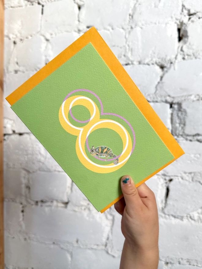 a bright green card with a big yellow number 8 and an illustrated chameleon with a bright yellow envelope