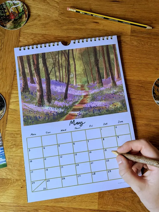 Illustrated wall calendar showing the month of May, with an artwork of the bluebell woods