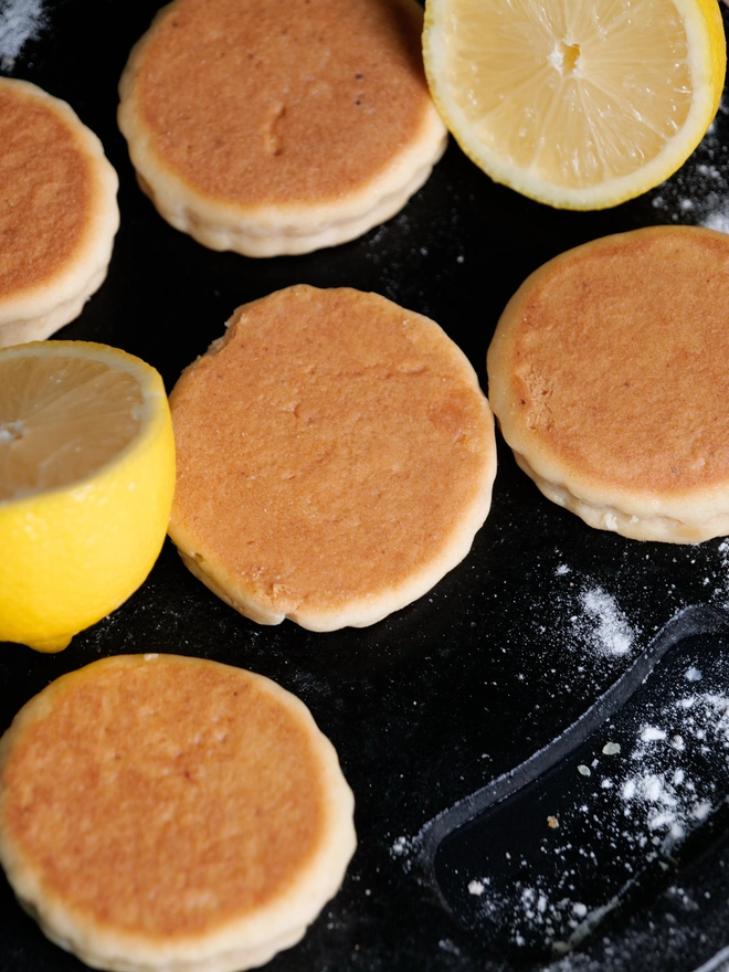 Lemon Welsh Cakes on a black griddle next to cut lemons