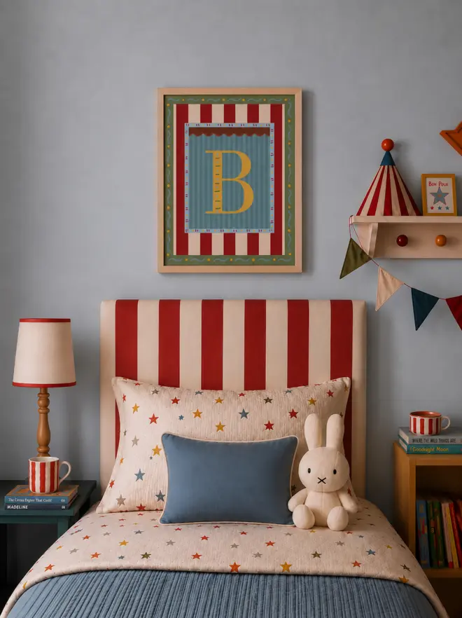 Framed vintage circus letter B print in mustard yellow, teal and red stripes, styled above a red and cream striped bed in a playful children’s bedroom.