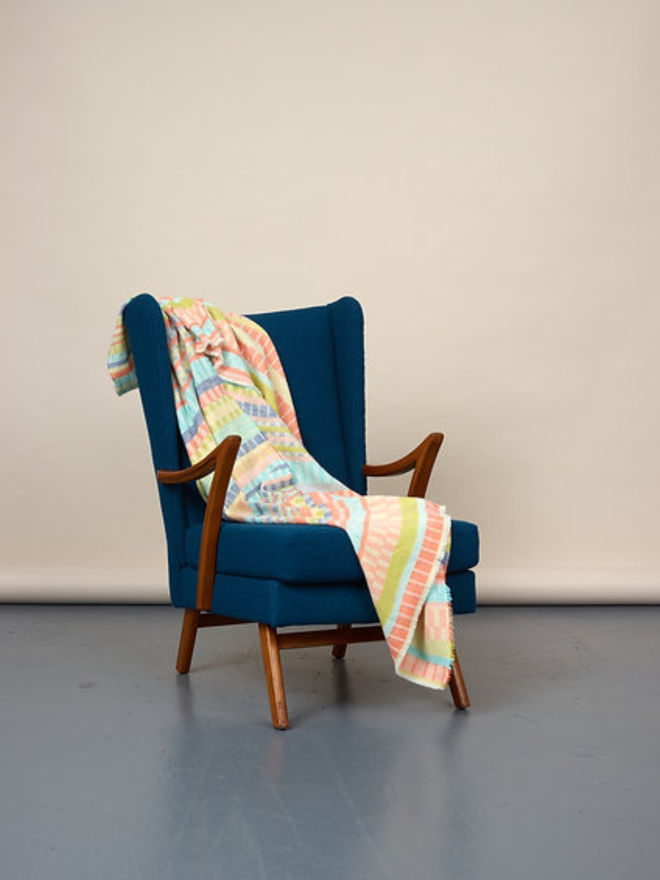indie lambswool blanket. a multicoloured blanket photographed thrown over a blue chair.