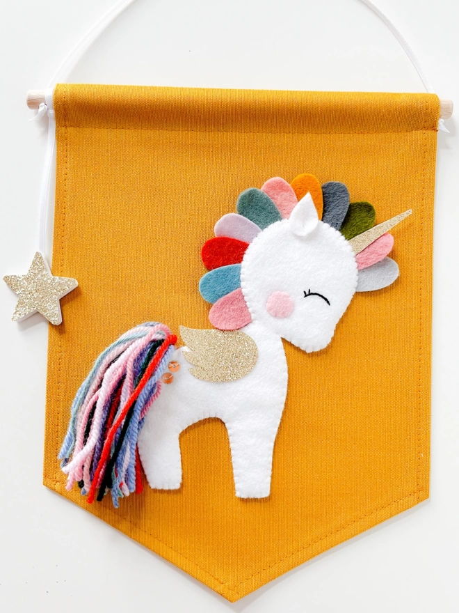 A white unicorn with multicoloured mane and tail on a mustard banner
