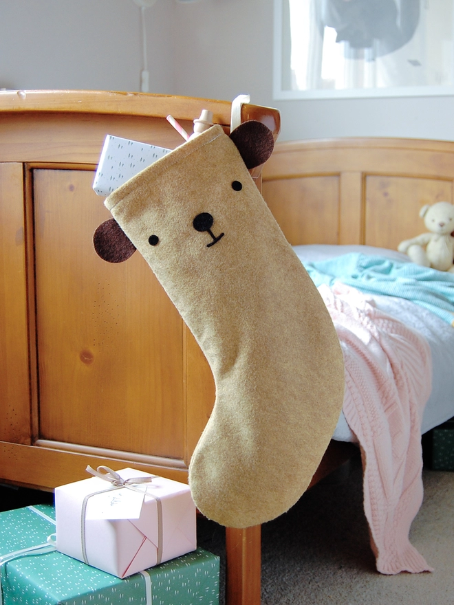 A handmade felt bear stocking hangs on the end of a wooden bed.